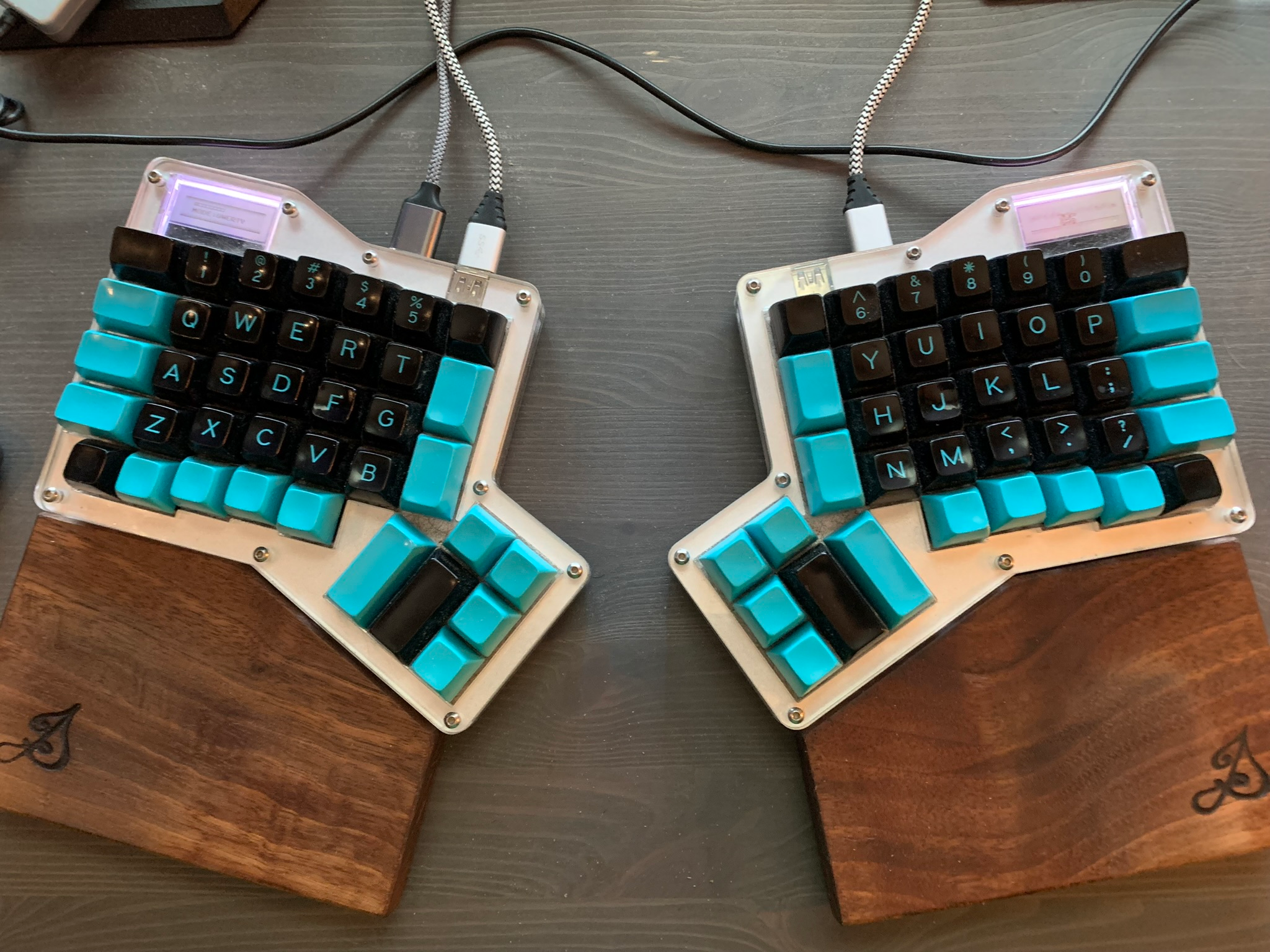 A photo of my Ergodox Infinity split keyboard. The keys are mostly black with cyan legends and a few cyan keys. There are two wrist rests made from walnut and branded by my woodworking maker's mark.