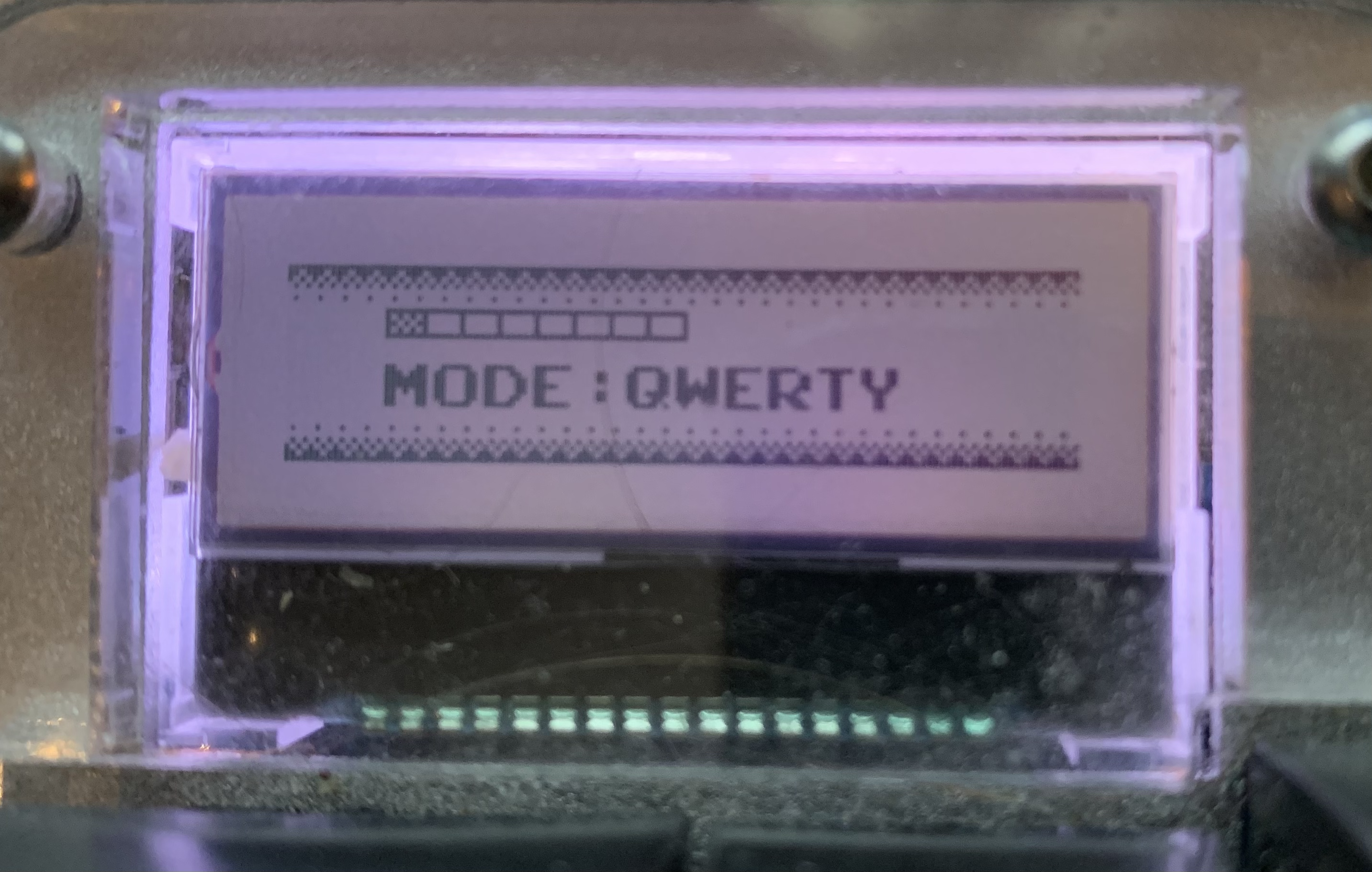 A photo of an LCD display showing the words "Mode: Qwerty" with some pixel art styling.